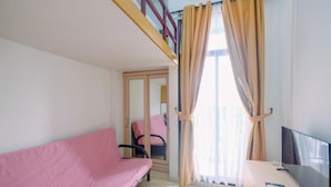 Ein Zimmer mit einem rosafarbenen Sofa, einem Fernseher auf einem Schrank und einem Fenster mit Vorhängen.