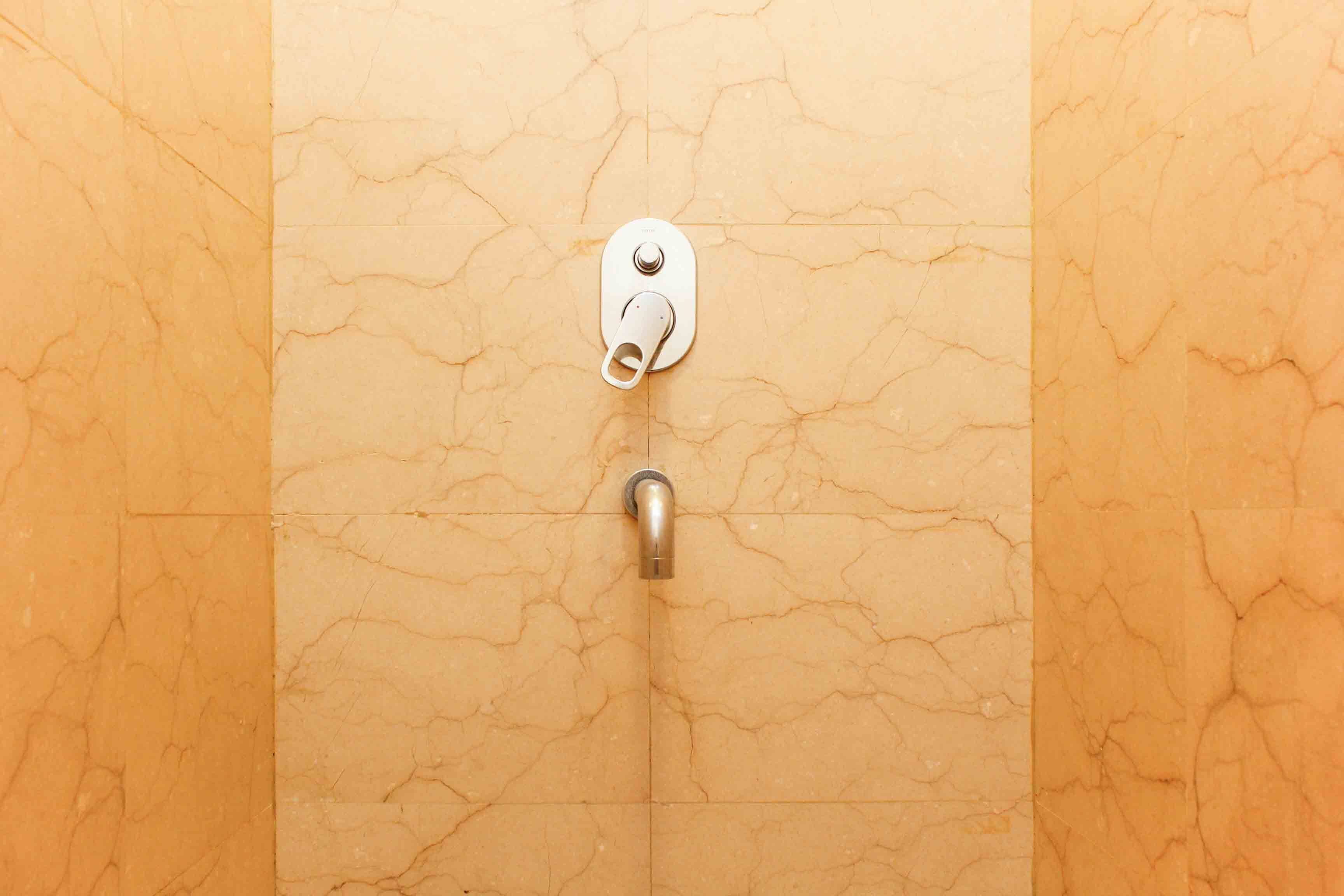 A bathroom with a marble wall and a metal faucet.