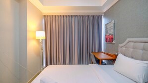 A hotel room with a neatly made bed, a bedside table with a lamp, a chair, and a wall-mounted artwork.