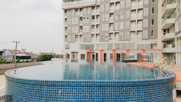 A modern building with a rooftop swimming pool, featuring a clear sky and a view of the surrounding area. - Comfy Studio At Amazana Serpong Apartment (South Tangerang)