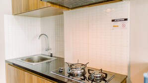 A kitchen with a stainless steel sink, a gas stove, and wooden cabinets. - Comfy Studio At Amazana Serpong Apartment (South Tangerang)