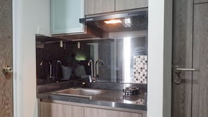 A compact kitchen with a stainless steel sink, a black range hood, and wooden cabinets. - Cozy Stay Studio Apartment At Taman Melati Surabaya (Surabaya)