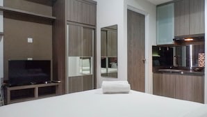 A modern hotel room with a bed, a television, a mirror, and a kitchenette. - Cozy Stay Studio Apartment At Taman Melati Surabaya (Surabaya)
