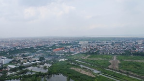 A cityscape with a mix of residential and commercial buildings, a river, and a large open area with a dirt path. - Cozy Stay Studio Apartment At Taman Melati Surabaya (Surabaya)