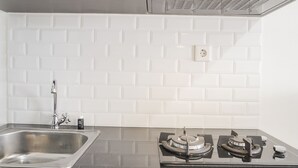 A kitchen with a stainless steel sink, a gas stove, and white subway tile backsplash. - Stunning Studio Apartment At Belmont Residence Puri (Jakarta)