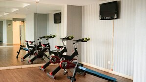 A gym with stationary bikes, mirrors, and a TV on the wall. - Stunning Studio Apartment At Belmont Residence Puri (Jakarta)