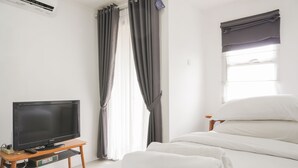 A hotel room with a bed, a TV on a wooden stand, and a window with curtains. - Stunning Studio Apartment At Belmont Residence Puri (Jakarta)