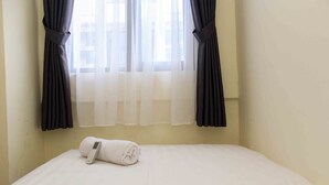 A hotel room with a bed, a remote control, and sheer curtains. - Comfort And Serene 2Br At Meikarta Apartment (Cikarang)