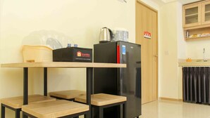 A kitchenette with a black refrigerator, a coffee maker, and a travelello sign. There are two wooden tables and a black cabinet above the refrigerator. - Comfort And Serene 2Br At Meikarta Apartment (Cikarang)