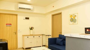 A hotel room with a wooden door, a white cabinet, a blue sofa, a white coffee table, and a reception desk. - Comfortable And Spacious 2Br At Meikarta Apartment (Cikarang)