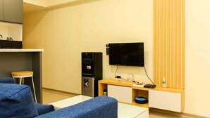 A compact living space with a sofa, a small table, a TV, a mini-fridge, and a wooden cabinet with a vertical slat design. - Comfortable And Spacious 2Br At Meikarta Apartment (Cikarang)