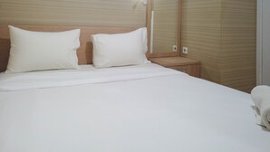 Una cama bien hecha con sábanas y almohadas blancas, una mesita de noche con lámpara y un cabecero de madera.