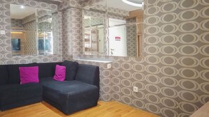 Una sala de estar con un sofá seccional, un muro espejado y papel tapiz estampado.