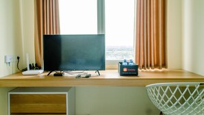 Une chambre d’hôtel avec un bureau en bois, un téléviseur à écran plat, un ordinateur portable, une multiprise, une bouteille d’eau et une chaise blanche.