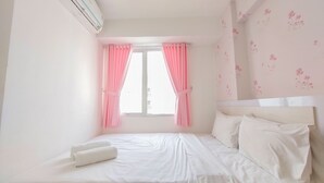 A neatly made bed with white linens and pillows, a window with pink curtains, and a wall with a floral pattern. - Comfort 2Br Apartment At Bassura City (Jakarta)
