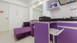 A compact living space with a purple sofa, a small kitchenette, and a mirror above the counter. - Comfort 2Br Apartment At Bassura City (Jakarta)