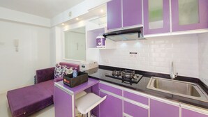A compact kitchen with purple cabinets, a sink, and a small dining area with a purple sofa. - Comfort 2Br Apartment At Bassura City (Jakarta)
