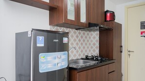 A compact kitchen with a refrigerator, a gas stove, wooden cabinets, and a patterned backsplash. - Comfort And Warm Studio Room Apartment At M-Town Residence (Gading Serpong)