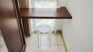A corner room with a wooden desk, a white chair, and a window with blinds. - Comfort And Warm Studio Room Apartment At M-Town Residence (Gading Serpong)
