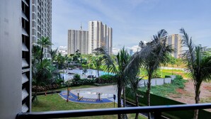 A view from a balcony overlooking a residential area with high-rise buildings, a swimming pool, and well-maintained greenery. - Elegant And Comfy Studio At Sky House Bsd Apartment (Pagedangan)