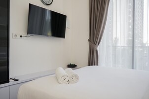 Quarto de hotel com cama, televisão presa na parede, relógio e janela com cortinas.