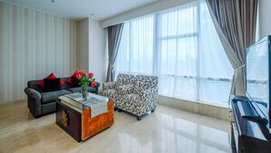 A modern living room with a sofa, a patterned armchair, a glass coffee table, and a piano. - New Furnished And Comfortable 2Br At The Mayflower Apartment (Jakarta)