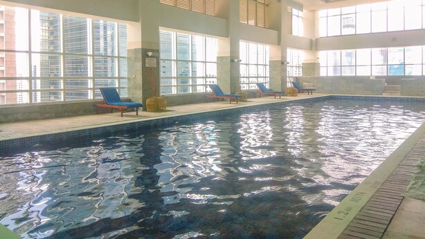 An indoor swimming pool with clear water, sunlit by large windows, and lounge chairs along the poolside. - New Furnished And Comfortable 2Br At The Mayflower Apartment (Jakarta)