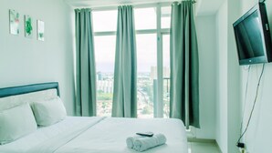 A hotel room with a bed, a TV mounted on the wall, and a window with curtains. - Nice And Cozy Studio At Tree Park City Apartment (Tangerang)