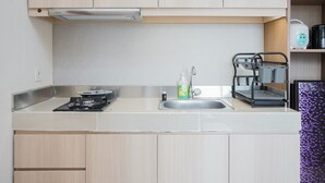 A modern kitchen with light wood cabinets, a stainless steel sink, a gas stove, and a kettle on the countertop. - Minimalist And Comfort 1Br At B Residence (Pagedangan)