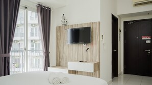 Habitación de hotel con una cama, un televisor montado, un estante de madera pequeño y una puerta.
