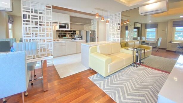 A modern living room with a sofa, coffee table, and a dining area with chairs. A kitchen is visible in the background.