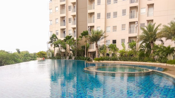 Una piscina con borde de azulejos, rodeada de palmeras y un edificio de varios pisos al fondo.