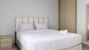 Een keurig opgemaakt bed met witte lakens en kussens, een houten garderobe en een klein nachtkastje met lades.