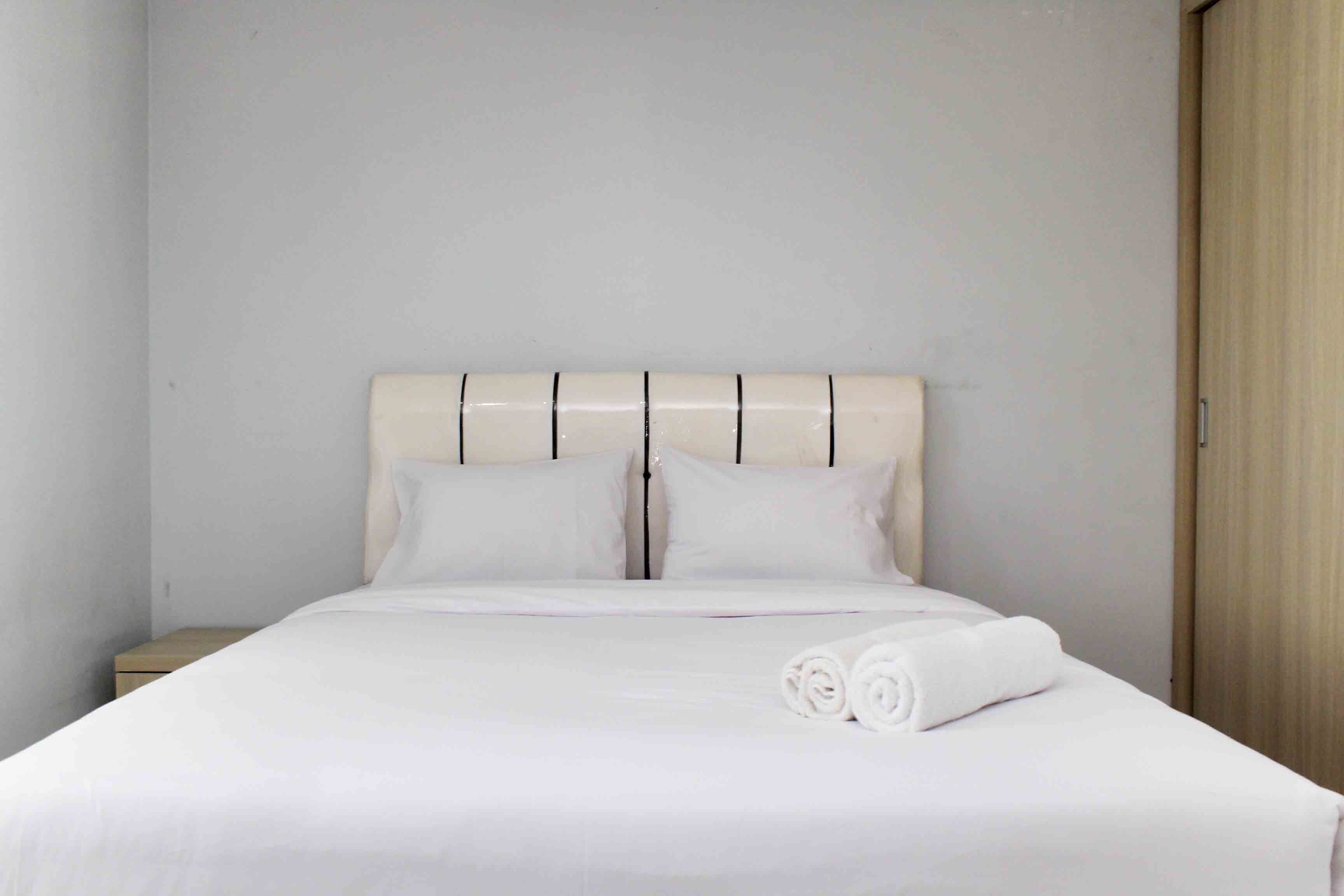 A neatly made bed with white linens and pillows, a wooden nightstand to the left, and a wooden wardrobe to the right.