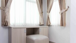 Een kamer met een licht houten bureau, een beklede kruk en gordijnen die open zijn getrokken om een raam te laten zien.