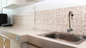 A kitchen with a stainless steel sink, beige tiled backsplash, and wooden cabinets.