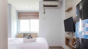 A hotel room with a bed, an air conditioner, a television, and a minibar.