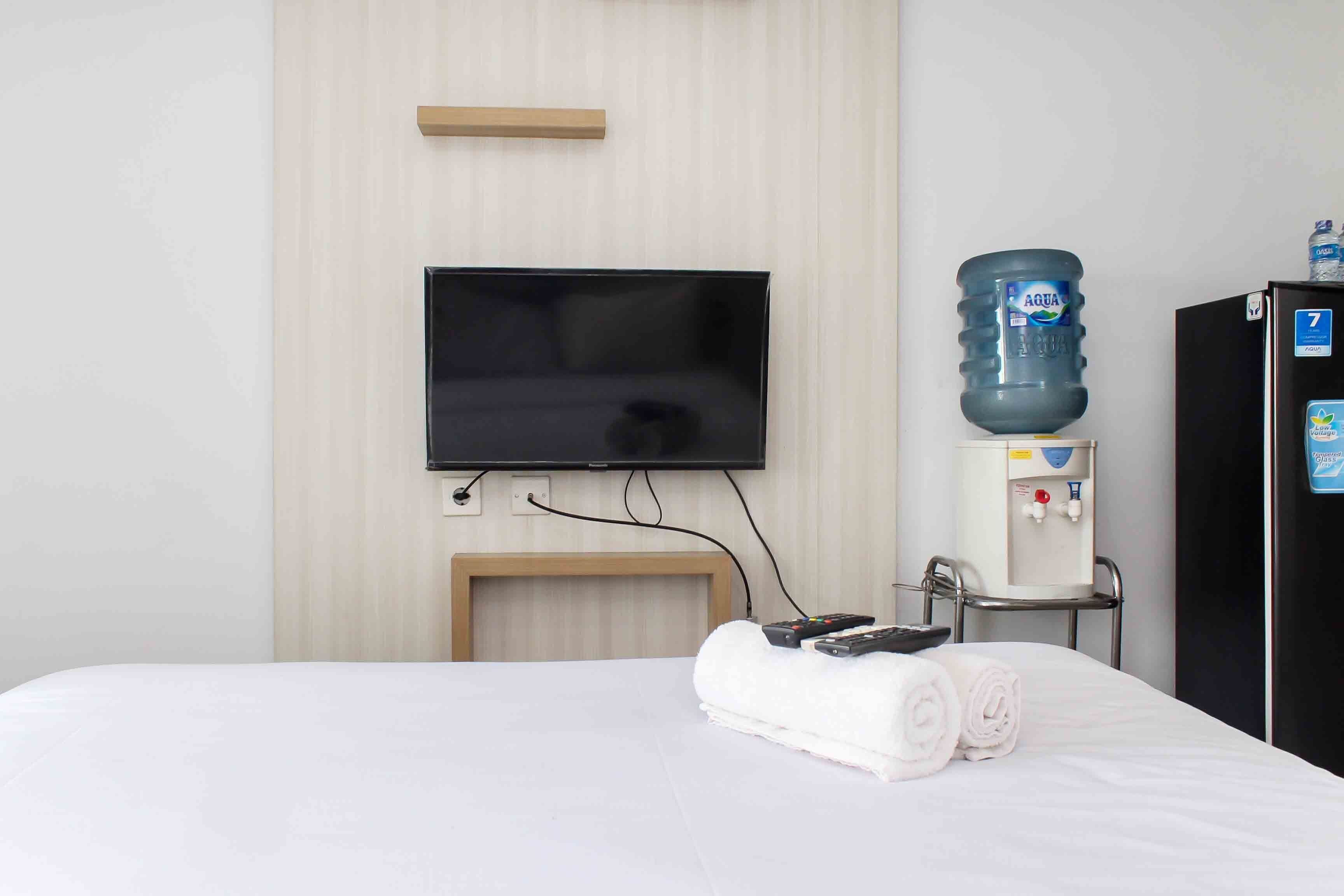 A hotel room with a bed, a television mounted on the wall, a water dispenser, and a refrigerator.