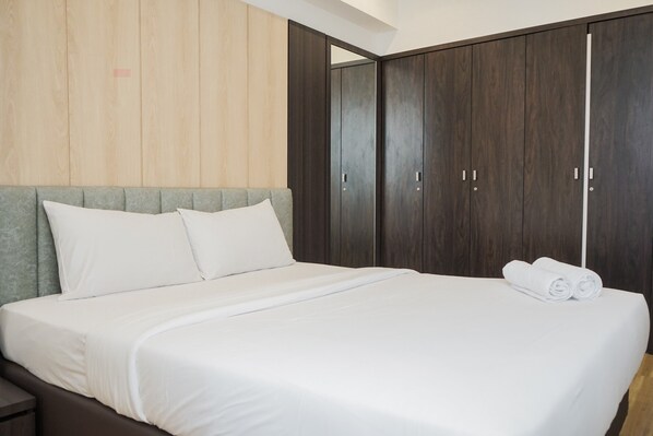 A neatly made bed with white linens, a grey headboard, and a pair of rolled towels on the foot of the bed.