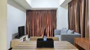 A modern living room with a wooden dining table, grey sofa, and a TV on a stand. - Big And Comfy 3Br At Vida View Apartement (Makassar)