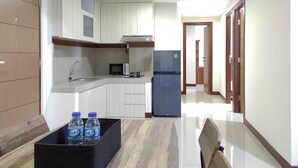 A modern kitchen with white cabinets, a microwave, a refrigerator, and a dining area with a table and chairs. - Big And Comfy 3Br At Vida View Apartement (Makassar)