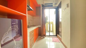 A kitchen with orange cabinets, a white countertop, and a sliding glass door leading to a balcony. - Spacious Studio Apartment At Gateway Ahmad Yani Cicadas (Bandung)