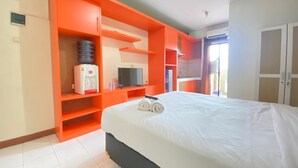 A hotel room with a large bed, orange storage units, a television, and a water dispenser. - Spacious Studio Apartment At Gateway Ahmad Yani Cicadas (Bandung)