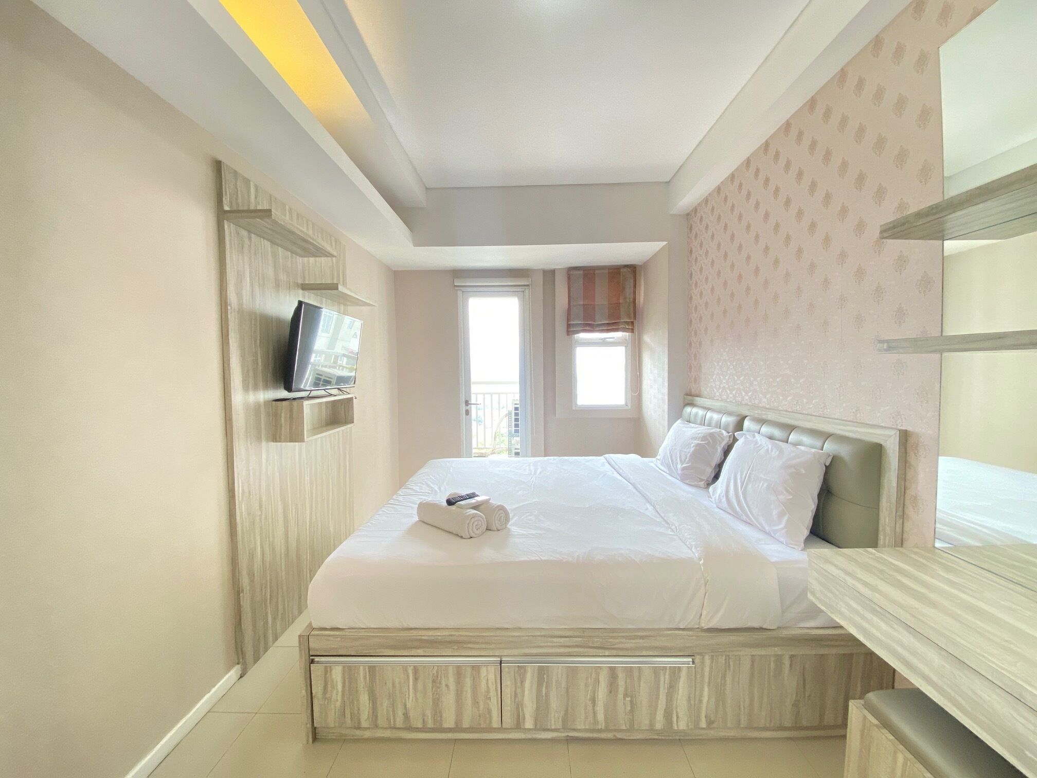 A hotel room with a bed, a television mounted on the wall, and a window with a view of the outside.