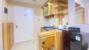 A compact kitchen with wooden cabinets, a gas stove, and a refrigerator. - Nice And Cozy 2Br Apartment At Parahyangan Residence (Bandung)