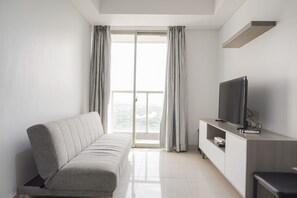A modern living room with a sofa, a TV, and a sliding glass door leading to a balcony.