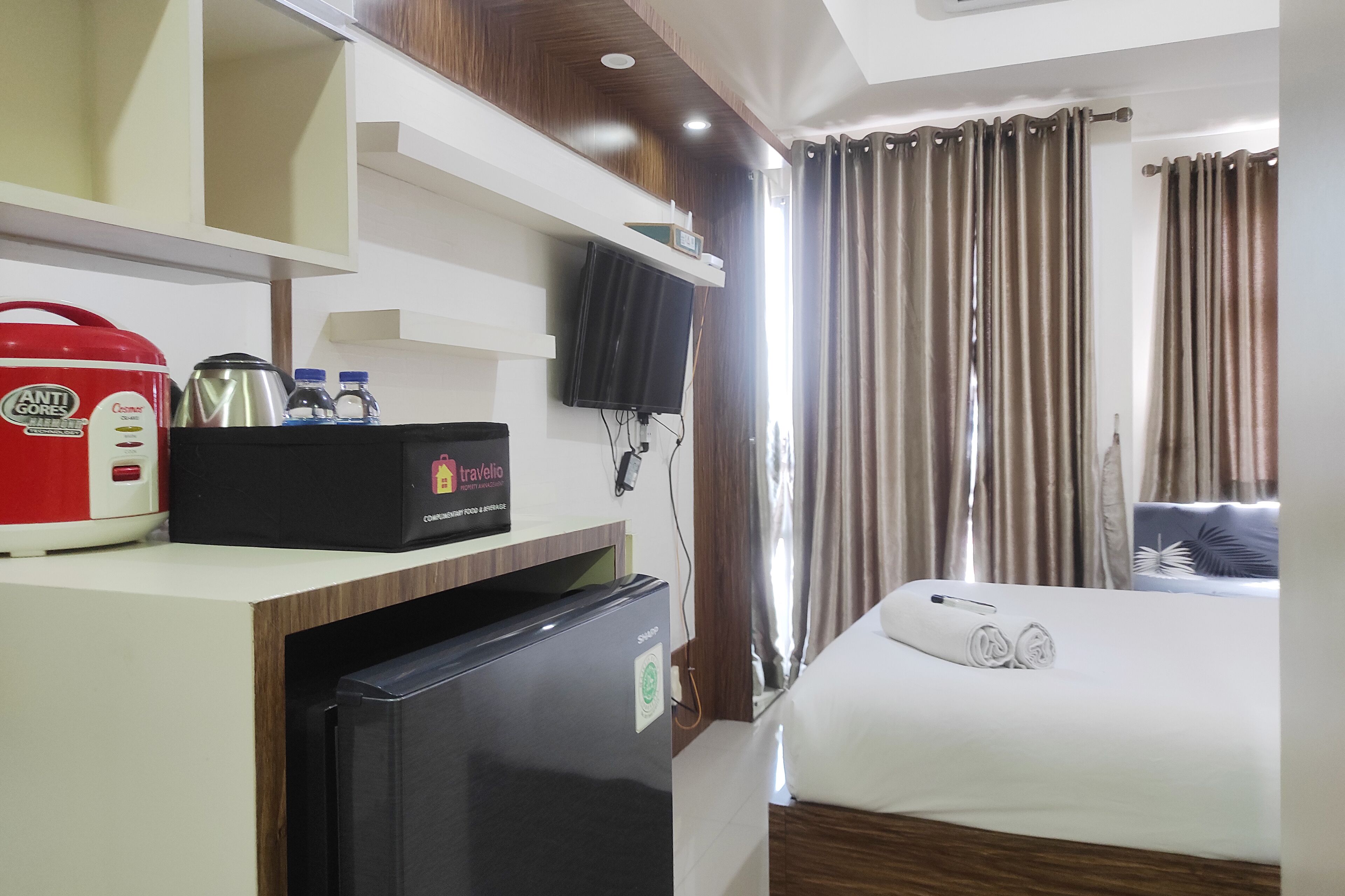 A hotel room with a bed, a TV, a minibar, and a refrigerator.