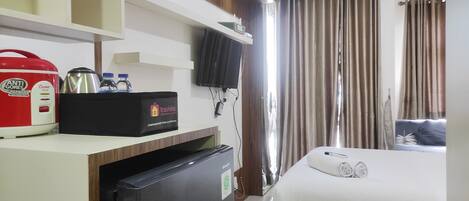 A hotel room with a bed, a TV, a minibar, and a refrigerator.