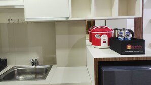 A kitchen with a stainless steel sink, white cabinets, a red electric kettle, a coffee maker, and a box labeled 'travelio' with beverages. - Convenient Studio At Vida View Makassar (Makassar)