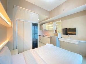 A modern hotel room with a large bed, a built-in wardrobe, a kitchenette, and a flat-screen TV.